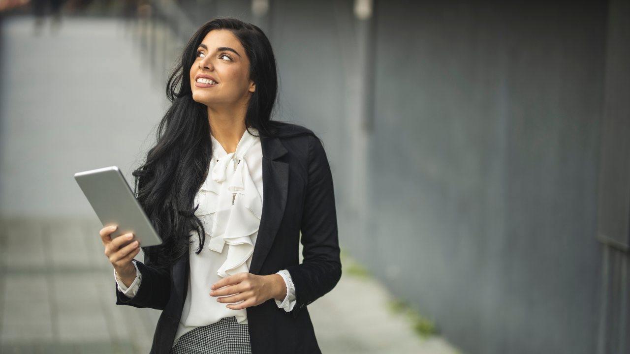 Woman in business attire holding a tablet outdoors, smiling—illustrating mobile-first salon consent and intake forms on the go.