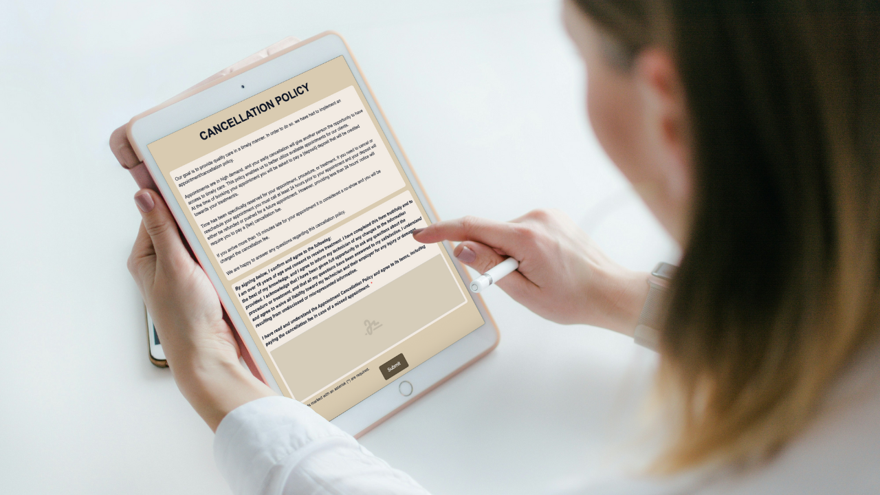 Glow Forms Blog Writer said:  Client signing a Glow Forms Cancellation Policy on a tablet—clear deposit, 24-hour notice, and late-cancel/no-show fee terms visible.