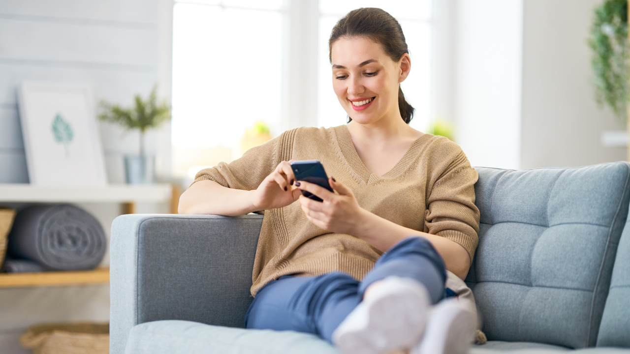 Client completing a Glow Forms online form on her phone at home, relaxing on a sofa before her salon appointment.