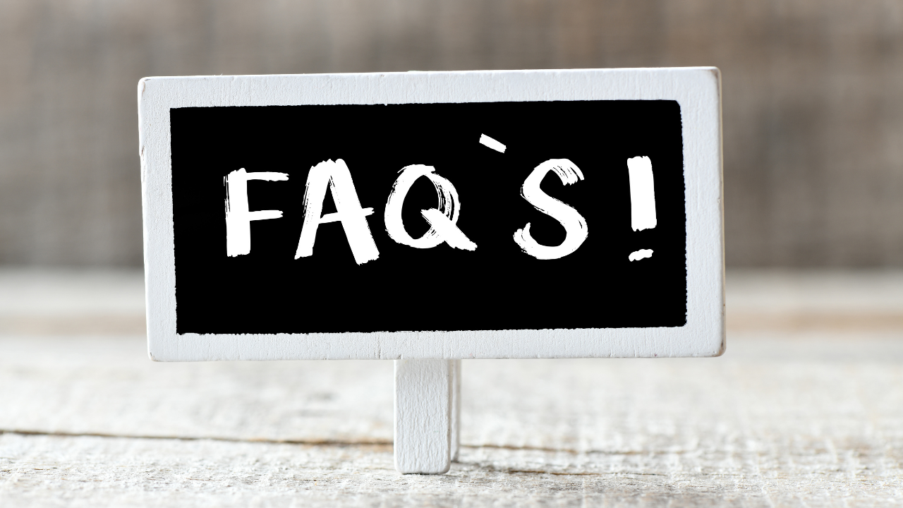 Chalkboard sign reading “FAQ’s!” on a wooden table, symbolizing a clear salon FAQ page clients can read before appointments.