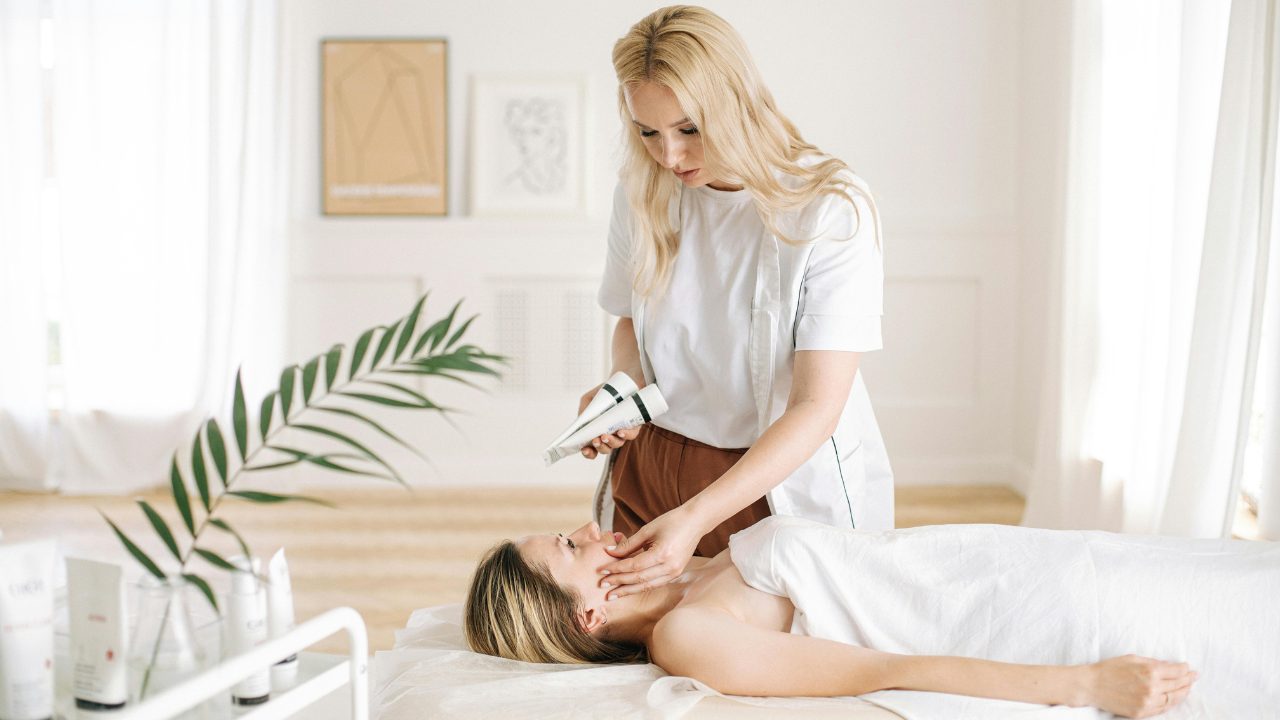 Esthetician performing a facial treatment in a bright spa, applying skincare to a regular client on a treatment bed during a professional beauty service.