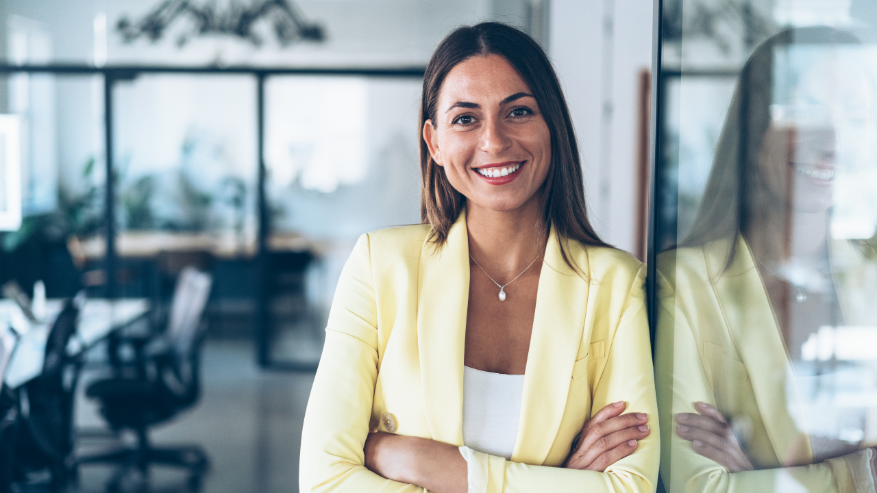 Salon owner in a bright studio, smiling with arms crossed, planning midyear updates to Glow Forms client consent forms.