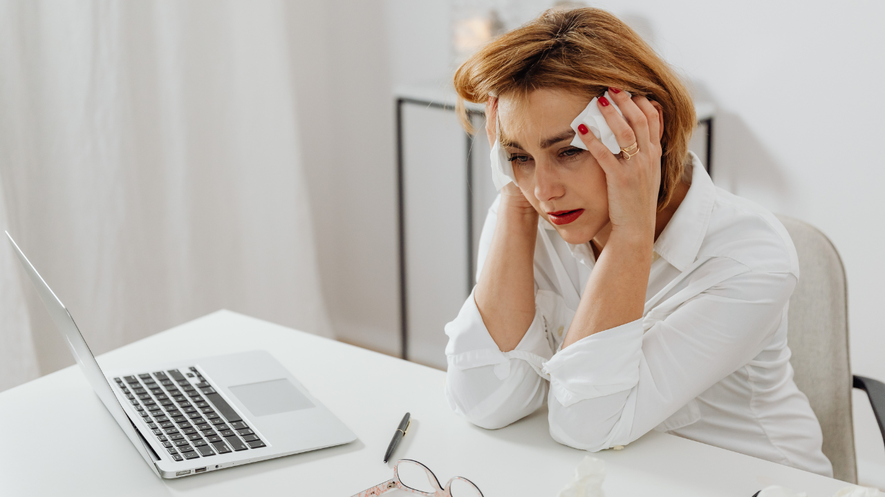 Beauty professional looks exhausted at her laptop, holding her head—burnout from admin and paperwork.