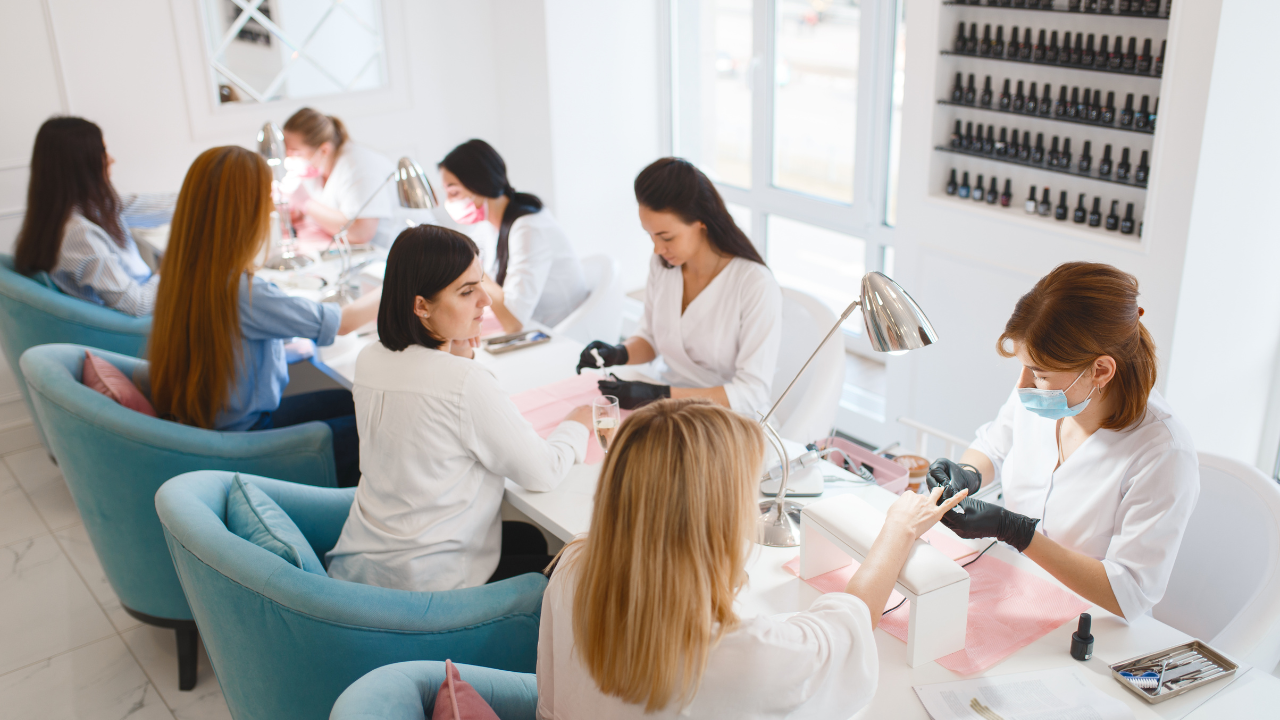 Full nail salon in session—technicians serve clients at several manicure tables, showing steady bookings.