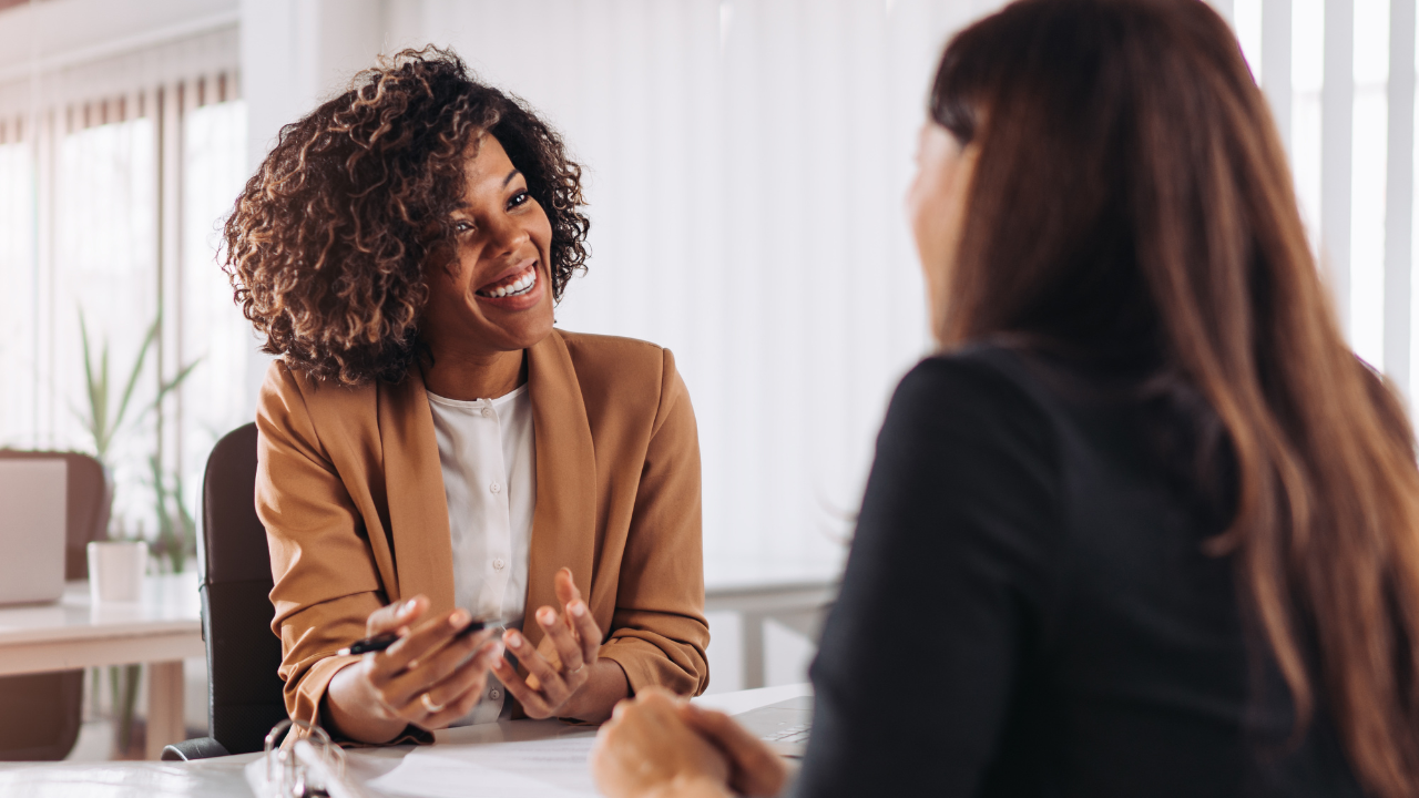 Stylist smiles and takes notes while a client shares concerns—showing attentive, client-centered communication.