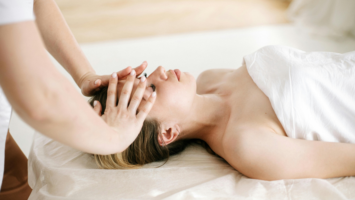 Beauty professional gently massages a client’s forehead during a refreshed facial protocol—calm studio setting.